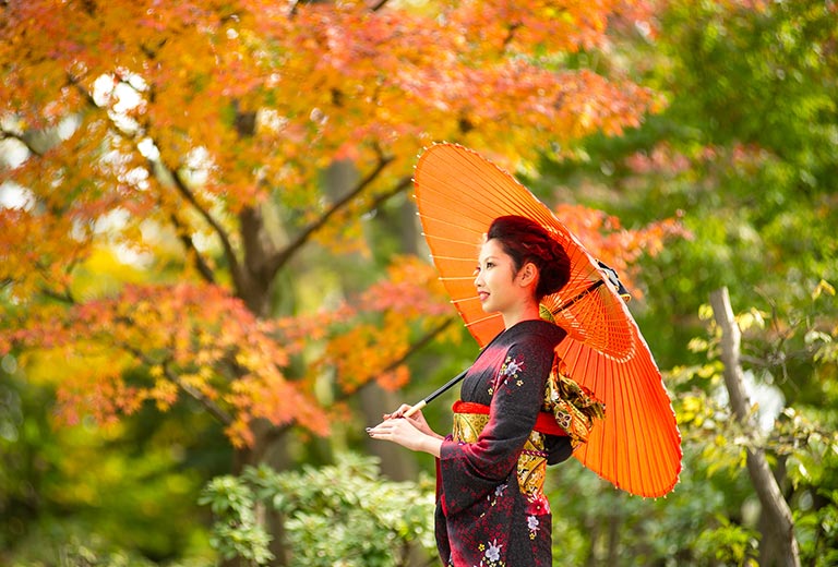 紅葉の下で、振袖を着た女性が傘をさす様子